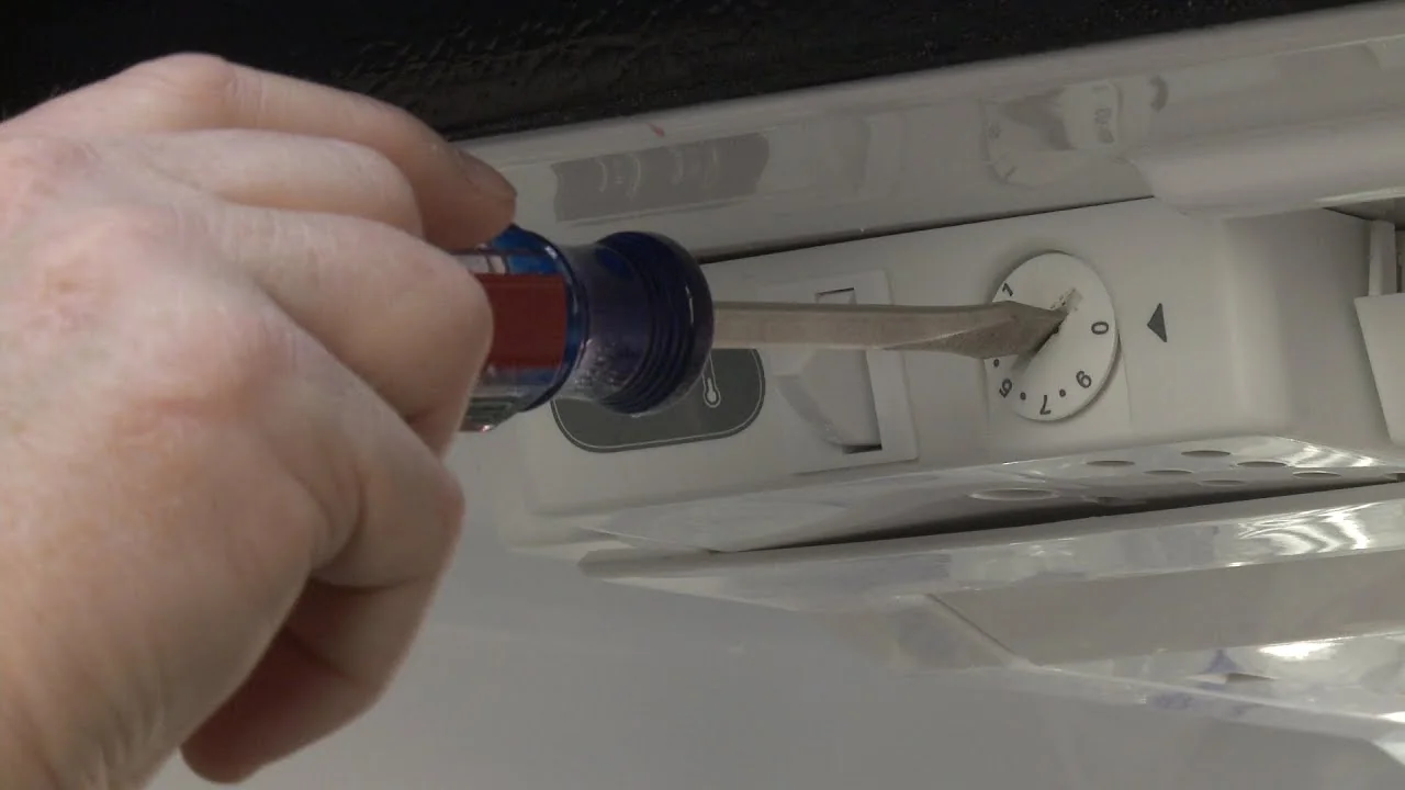 Close-up of a refrigerator temperature-control dial and thermostat housing during inspection